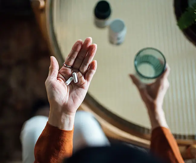 Hände von oben, die Tabletten und ein Wasserglas halten.