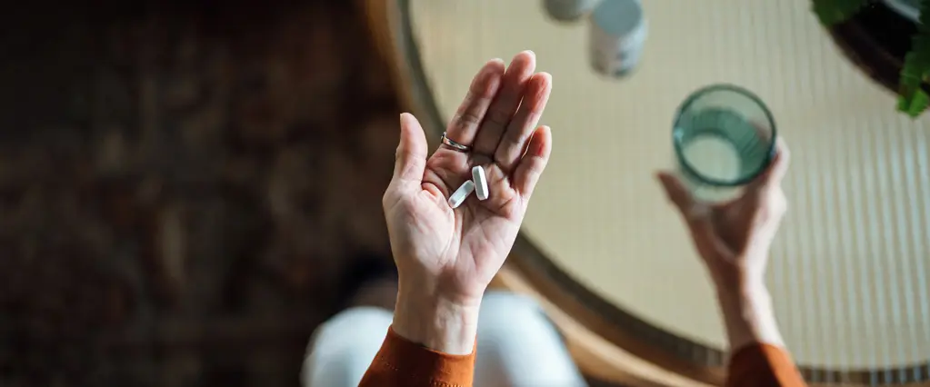 Hände von oben, die Tabletten und ein Wasserglas halten.