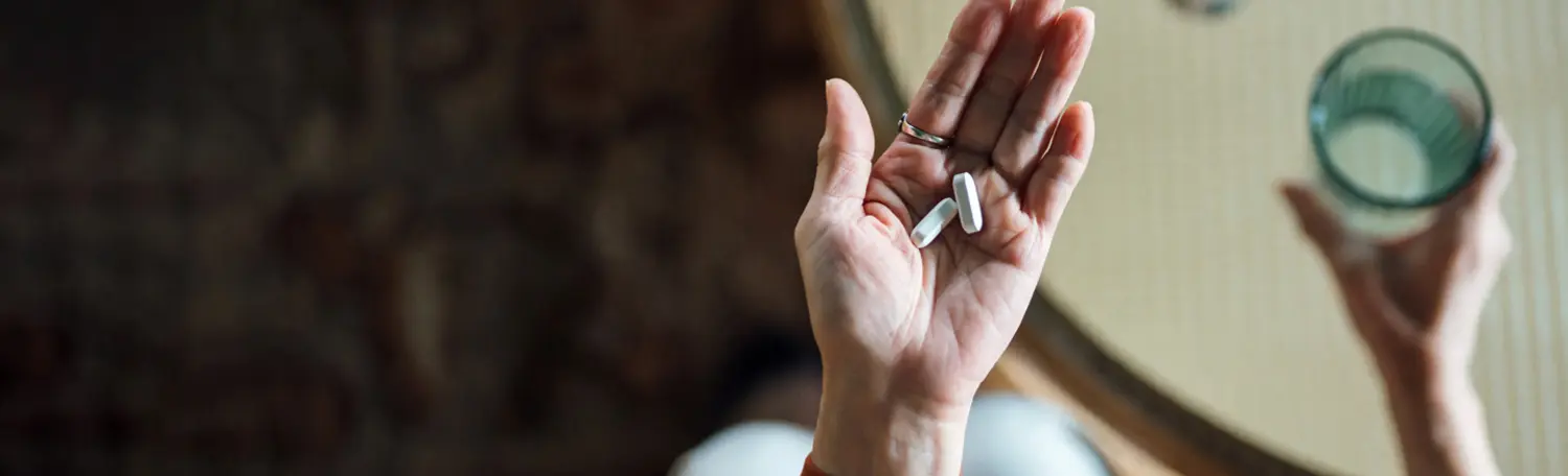 Hände von oben, die Tabletten und ein Wasserglas halten.