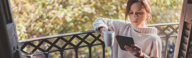 Frau sitzt auf Balkon und liest mit E-Reader