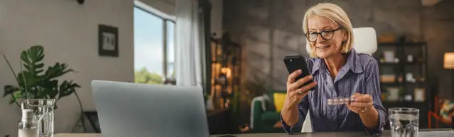 Frau mit Medikament und Handy am Tisch
