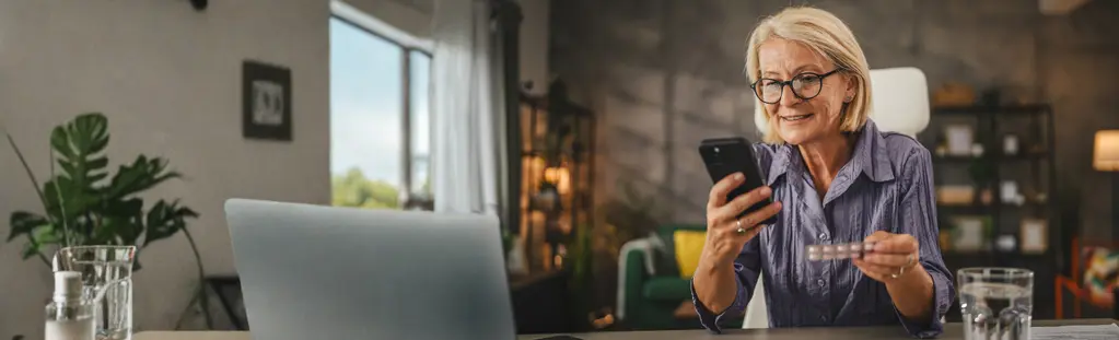 Frau mit Medikament und Handy am Tisch