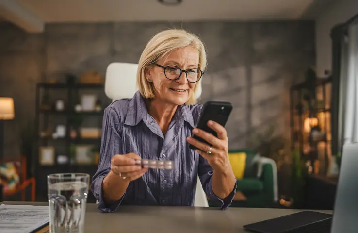 Frau mit Medikament und Handy am Tisch