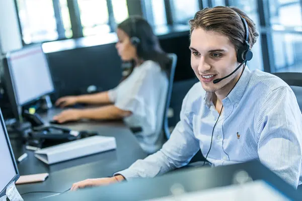 Technischer Support Manager mit Headset sitzt neben Kollegin am PC