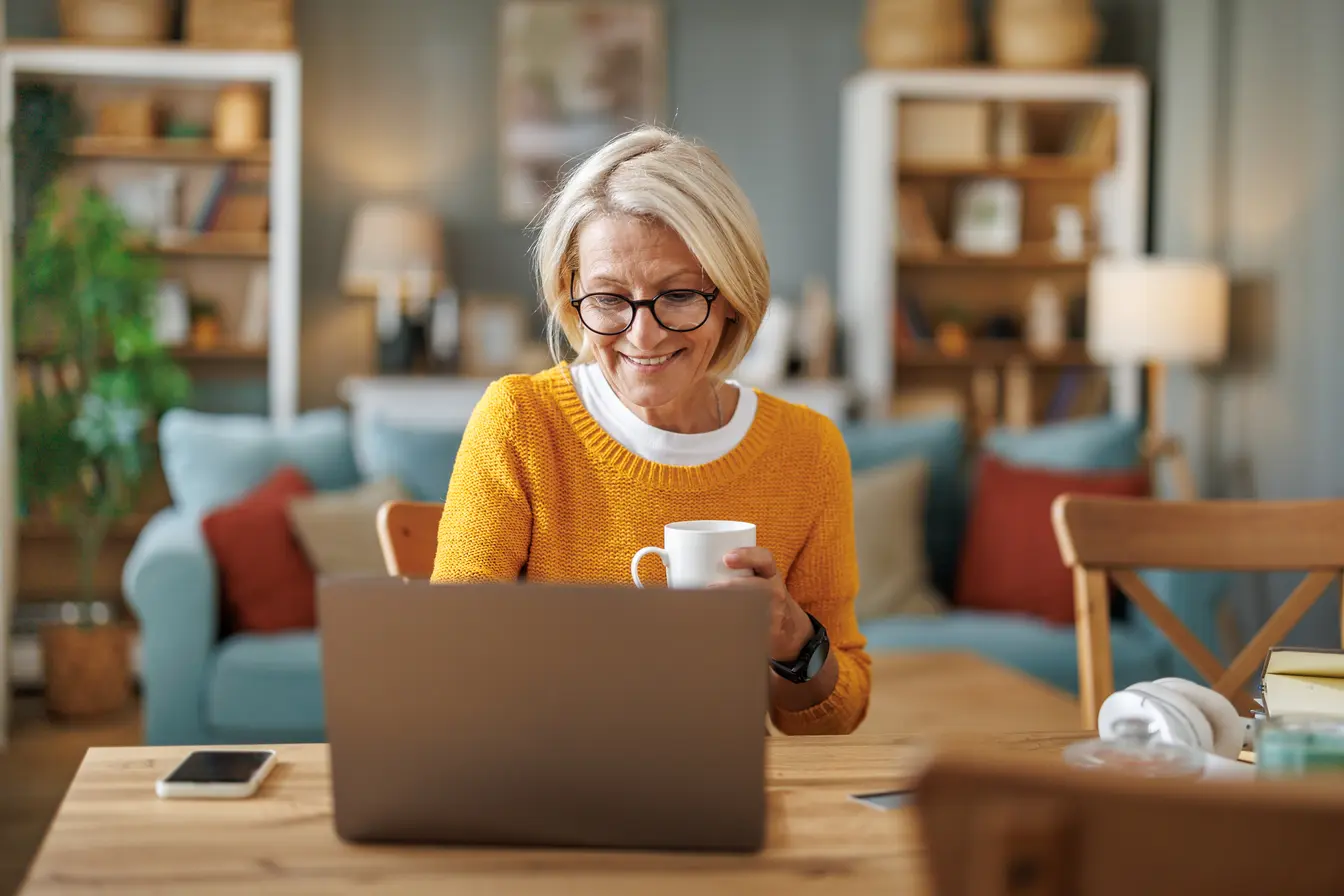 Frau mit Kaffeetasse und Laptop am Tisch