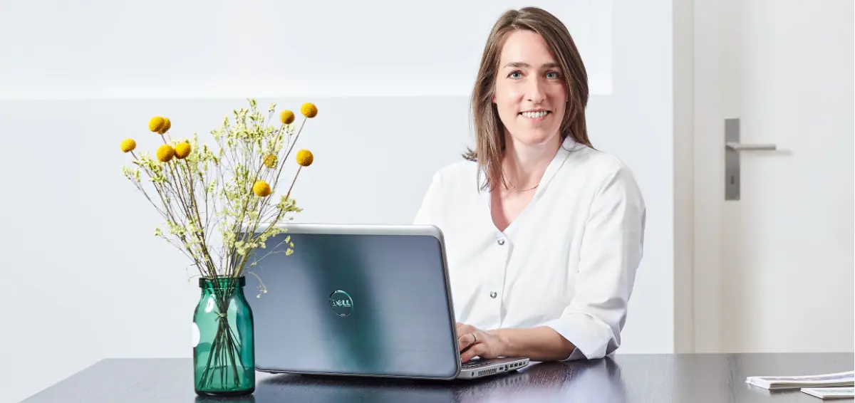 Ärztin sitzt am Tisch und benutzt Laptop