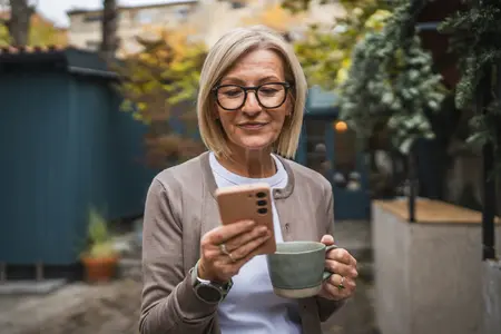 Frau im Hof mit Kaffeetasse und Handy