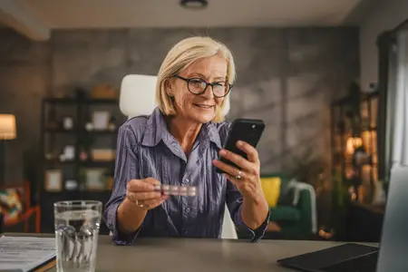 Frau mit Medikament und Handy am Tisch